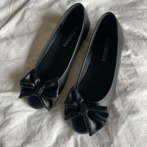 Svarta ballerinaskor med rosett - Super söta svarta ballerinaskor från Boohoo med en stor dekorativ rosett framtill. Storlek 36 men passar mig som annars har 37💞pris kan diskuteras                                         (Aldrig använda)