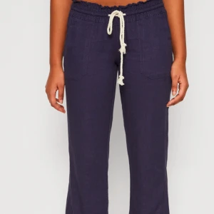 Mörkblå linnebyxor från Roxy med snörning - Säljer ett par mörkblå linnebyxor från Roxy i storlek M. Vit snörning i midjan och två framfickor. Byxorna har avslappnad passform och resår i midjan för extra komfort. Säljer då de aldrig kommer till användning. Beställt från Zalando. Jag är 165 cm. 