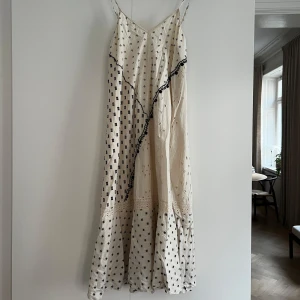 Vit långklänning med mönster från Zara - Säljer en vit långklänning från Zara med tunna axelband och mörkblåa mönster. Klänningen har spetsdetalj och volang nertill samt en dekorativ sned svart linje framtill. Perfekt för sommarens tillfällen! Storlek xs.