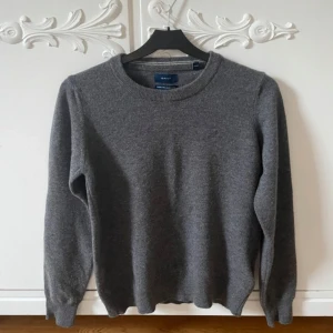 Grå ulltröja från GANT - Säljer en stilren grå tröja från GANT i superfin lammull. Tröjan har en klassisk rund halsringning och långa ärmar. Den är tillverkad i 100% lammull. Passar utmärkt för både vardag och mer uppklädda tillfällen.