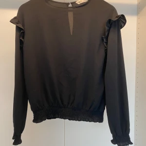 Blus med volanger - Svart blus med volanger. Är i super fint skick och är ursprungligen i storlek 158 men passar XS mer.