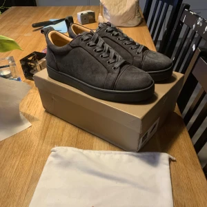 Skor från Christian Louboutin - Snygga grå sneakers i mocka från Christian Louboutin med den ikoniska röda sulan. Skorna har snörning och en stilren design som passar perfekt för en trendig look. Skriv priv om frågor eller annat!