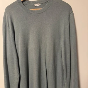 Blå/grön stickad tröja från Filippa K - Säljer en stilren  stickad tröja från Filippa K. Tröjan har en rund halsringning och långa ärmar, perfekt för kyligare dagar. Den är mjuk och bekväm, idealisk för både vardag och avslappnade tillfällen.
