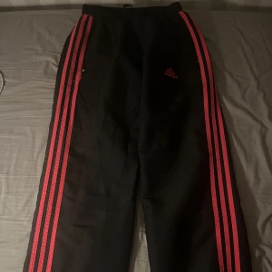 Svarta Adidasbyxor med rosa linjer  - Säljer ett par svarta träningsbyxor från Adidas med röda ränder längs sidorna. Byxorna har en normal passform och är perfekta för träning. De har en elastisk midja för extra komfort.