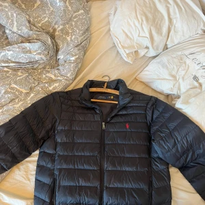 Svart dunjacka från Polo Ralph Lauren - Säljer en stilren svart dunjacka från Polo Ralph Lauren. Jackan har en dragkedja framtill och är långärmad. Perfekt för våren. Knappt använd och storlek L