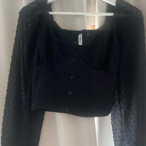 Svart prickig blus från FB Sister - Säljer en svart blus från FB Sister med prickigt mönster och knappar framtill. Blusen har långa ärmar och en croppad passform. Perfekt för en stilren look! Köpte toppen för 500 så väldigt bra pris på den