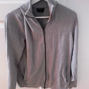 Grå kofta från Massimo Dutti - Säljer en stilren grå kofta från Massimo Dutti i extrafin bomull. Koftan har en dragkedja framtill och ribbade detaljer vid krage och ärmslut. Perfekt för en avslappnad men elegant look. Skick 9/10. Tveka inte att skriva