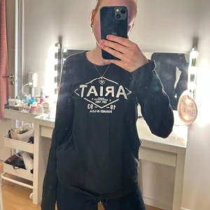 Svart långärmad tröja från Ariat - Säljer en svart långärmad tröja från Ariat med vit text och grafisk design på framsidan. Perfekt för en avslappnad stil. Tröjan har en rund halsringning och är tillverkad i ett mjukt material.💞