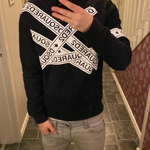 Svart tröja från Dsquared2 - Säljer en svart tröja från Dsquared2 med vita band som korsar över bröstet och ärmarna. Tröjan har långa ärmar och en normal passform. Perfekt för en stilren look. Har några fläckar men tvättar den innan du köper