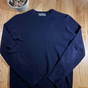 Mörkblå stickad tröja - Säljer en stilren mörkblå stickad Tröja nu har en texturerad yta och långa ärmar med ribbade muddar vid ärmslut och nederkant. Perfekt för kyligare & soliga dagar! Tröjan är mörk marinblå👍