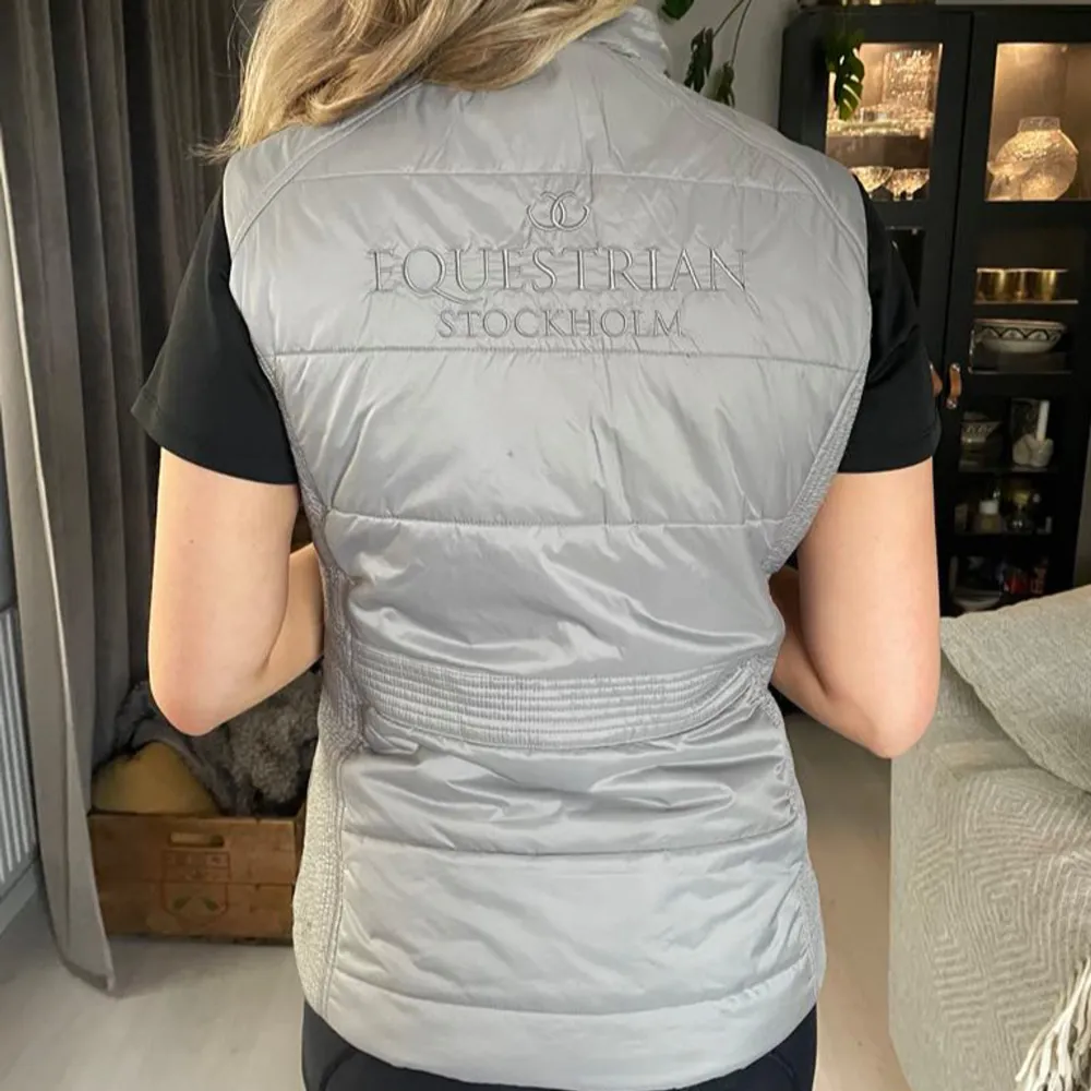 Snygg grå dunväst från Equestrian Stockholm med dragkedja framtill och två praktiska fickor med dragkedjor. Perfekt att ha i stallet nu när det börjar bli varmare ute . Takit.