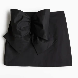 Svart kjol med stor rosett - Snygg svart kortkjol med en stor  rosett på framsidan. Den är i storlek L men sitter väldigt tajt på mig som när M. Skulle säga den sitter perfekt på en S 💖helt oanvänd !!