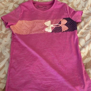 Rosa tränings t-shirt från Under Armour - Säljer en rosa tränings t-shirt från Under Armour. T-shirten är kortärmad och tillverkad i ett lätt och bekvämt material, perfekt för träning eller vardag. Passformen är loose för extra komfort. 🌟
