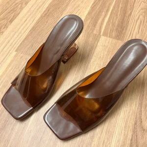 Bruna transparenta klackskor - Snygga bruna klackskor med transparent design och fyrkantig tå. Perfekta för en stilren look med en modern twist.