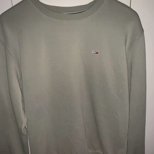 Grå sweatshirt från Tommy Jeans - Säljer en stilren grå sweatshirt från Tommy Jeans med deras ikoniska logga på bröstet. Tröjan har en rund hals och långa ärmar, perfekt för en avslappnad look. Passar bra till både jeans och joggers.