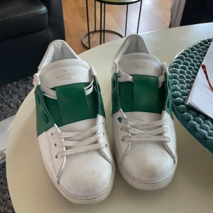 Valentino gröna - Snygga Valentino sneakers med en stilren design i vitt och grönt. Skorna har en bred grön rem över snörningen och är tillverkade i skinn. Perfekta för en trendig look.