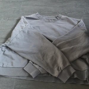 Grå sweatshirt från lager 157 - Säljer en stilren grå sweatshirt från lager 157. Tröjan har en klassisk rund hals och ribbade muddar vid ärmslut och nederkant. Perfekt för en avslappnad look. Passar både XS och S.