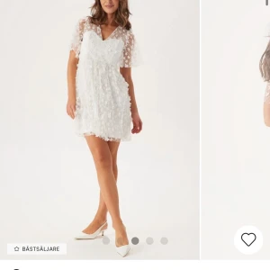 Studentklänning  - Söt vit klänning med blommigt mönster och v-ringad design. Den har korta ärmar och en luftig passform som ger en romantisk känsla. Perfekt för sommarens festligheter.