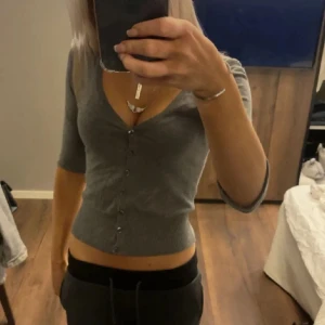 Grå ribbad kofta - Säljer en grå ribbad kofta med knappar framtill. Koftan har trekvartsärmar och en croppad passform. Säljer vidare den eftersom att jag aldrig använt den