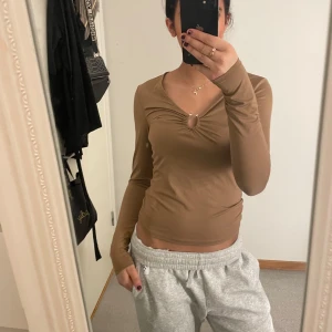 Brun långärmad topp - Säljer en brun långärmad topp med v-ringning och en snygg knytdetalj framtill. Perfekt för en stilren och bekväm look.