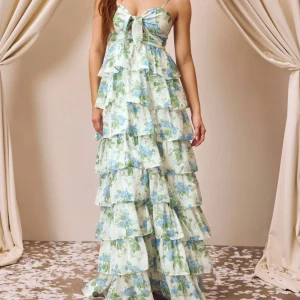 Blommig långklänning med volanger - Köpt för 957kr 🫶Säljer en romantisk långklänning med blommigt mönster i blått och grönt. Klänningen har smala axelband och en stor rosett framtill. Den är täckt av flera lager volanger som ger en luftig känsla. Perfekt för sommarens festligheter! Köpt från Cider🥰 Säljer då den inte passade mig🫶Endast testad på en gång ☝️ Aldrig använd annars 🫶Den blev lite skrynklig när den kom på posten, men löses enkelt med att stryka den.