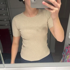 Beige ribbad topp - Säljer en stilren beige ribbad topp med korta ärmar. Perfekt för en enkel och snygg look. Passar bra till både jeans och kjol. S/M aldrig använd 
