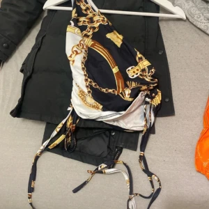 Mönstrad bikini med kedjedetaljer - Snygg topp med ett unikt mönster av kedjor i guld och vitt på en mörkblå bakgrund. Toppen har knytband och en stilren design som passar perfekt för sommardagar vid stranden.