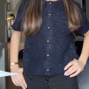 Mörkblå kofta med pärlknappar - Säljer en fluffig mörkblå kofta med korta ärmar och snygga pärlknappar framtill. Koftan har en mjuk och mysig känsla, perfekt att slänga på sig över en topp. Enkel och stilren design som passar till många outfits. endast använd en gång