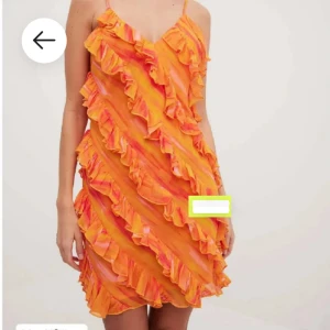 Orange volangklänning med smala axelband - Superfin kort klänning i orange och rosa toner med smala axelband och massor av volanger i diagonala rader. Sval och lätt, perfekt för sommarens alla tillfällen. V-ringad framtill och med ett färgglatt mönster som verkligen sticker ut
