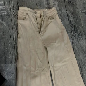 Beiga raka byxor från H&M Divided - Snygga beiga byxor från H&M Divided i rak modell. Klassisk femficksdesign med bälteshällor och dragkedja. Tillverkade i bomullsmix som känns mjuk och skön. Perfekta för en clean och stilren look.