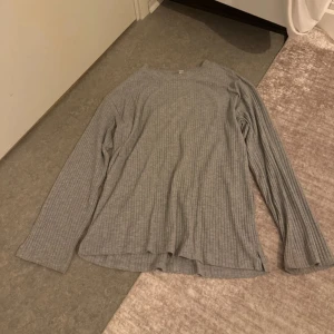 Grå ribbad långärmad tröja - En enkel och stilren grå långärmad tröja med ribbat tyg. Tröjan har rund halsringning och är i en mjuk, stretchig bomullsblandning. Perfekt för lager-på-lager och chill dagar. Passformen är normal och modellen är klassisk utan några extra detaljer.