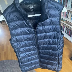 Blå dunväst från Uniqlo - Säljer en blå, quiltad dunväst från Uniqlo Ultra Light Down. Västen har hög krage, dragkedja framtill och är superlätt. Perfekt att slänga över en hoodie eller t-shirt för extra värme. Enkel och stilren design som funkar till det mesta.