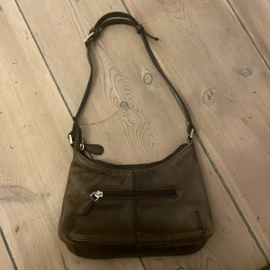 Brun axelväska i skinn från Boxca - Säljer en brun axelväska i äkta skinn från Boxca. Väskan har justerbar axelrem, dragkedja upptill och ett extra fack med dragkedja på framsidan. Insidan är fodrad i beige tyg och har ett innerfack med dragkedja. Perfekt storlek för vardagens essentials.