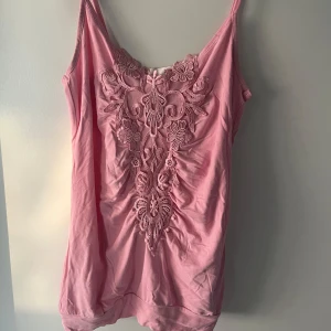 Rosa linnetopp med spetsdetaljer - Supersöt rosa linnetopp med tunna axelband och broderade spetsdetaljer framtill. Toppen har en feminin v-ringning och är perfekt för varma dagar. Mjuk och skön känsla tack vare bomullsmaterialet.