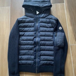 Ny Moncler Cardigan med luva - Moncler Cardigan i nyskick - aldrig använd. Storlek M men kan passa S. Väldigt clean och sällsynt modell. Den är gjord av skönt material och sitter sjukt bra på kroppen. Passar alla outfits och matchar med alla färger. Kan frakta samt mötas upp!