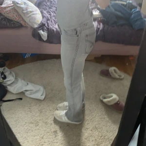 Ljusgrå bootcut jeans med slits - Säljer ett par ljusgrå jeans med bootcut passform och snygga slitsar vid bensluten. Jeansen har klassiska fickor och markerade sömmar. Perfekta för dig som gillar en avslappnad men trendig look. De är knappt använda! 