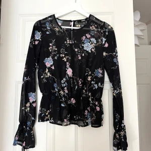 Blommig svart blus från Bik Bok - Supersöt svart blus från Bik Bok med blommigt mönster. Långärmad modell i mesh tyg och smock i midjan för en snygg siluett. Ärmarna har knytband vid handlederna för extra detalj. Endast använd en gång så nyskick!