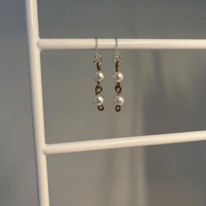 Brons/guld  örhängen med pärlor - Snygga örhängen med två vita pärlor på varje, uppträdda på en tunn guldig/brons kedja. Perfekta för att ge en elegant touch till din stil. Lätta att bära och passar till många olika looks. De är handgjorda!
