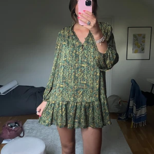 Grön blommig kortklänning med volang - Supersöt kortklänning i grönt med blommigt mönster och volang nertill. 