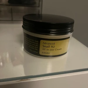 COSRX Advanced Snail 92 Cream - COSRX Advanced Snail 92 All in one Cream i en rund burk med svart lock. Innehåller 100g och är berikad med 92% snigelsekret för återfuktad och glowig hud. Perfekt för dig som vill ha en mjuk och fräsch känsla i ansiktet.