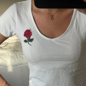 Vit croppad topp med rosbroderi - Superfin vit croppad topp från New yorker med v-ringning och korta ärmar. På bröstet sitter ett broderat rött ros-motiv. 🌹❤️