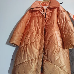 Orange pufferjacka från Guess, M - Snygg orange pufferjacka från Guess med quiltad design och dragkedja framtill. Jackan har hög krage och coolt mönstrat foder i orange och vitt. Tillverkad av återvunnen polyester, perfekt för kalla dagar när du vill sticka ut.