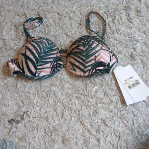 Grön och rosa bikiniöverdel med palmblad - Snygg bikiniöverdel med tropiskt palmbladsmönster i grönt och rosa. Kuporna är inte push och axelbanden är justerbara för perfekt passform. Perfekt för strandhäng och poolparty!