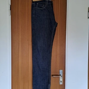 Mörkblå raka jeans i klassisk modell - Snygga mörkblå jeans med raka ben och klassisk femficksdesign. Jeansen har hög midja och är tillverkade i robust denim med kontrastsömmar. Perfekta för dig som gillar en tidlös och clean look.