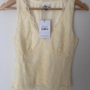 Ljusgul spetslinne från Princess Polly - Supersöt ljusgul linnetopp från Princess Polly med spetsdetaljer och v-ringning. Toppen är ärmlös, croppad och har fina spetskanter både upptill och nertill. I sista bilden kan man se en dragkedja som är placerad åt sidan av toppen (längs sömmen). Tyvärr var den för liten för mig och därför var jag tvungen att sälja den. Ordinarie pris var 45$, vilket är ungefär 438kr. OBS! Tänk på att jag har betalat för tull och skatt enligt USA:s villkor, men väljer att sälja toppen enligt enbart priset. 