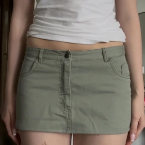 Grön minikjol med broderad blomma - Snygg grön minikjol i bomull med klassiska jeansfickor och bälteshällor. På baksidan finns en broderad blomma i samma färgton som kjolen, vilket ger en cool och unik detalj. Perfekt för dig som gillar en enkel men ändå personlig stil.          Storlek 38 men skulle säga att den passar 34/36🥰 mått rakt över midjan 37🥰pris kan diskuteras!