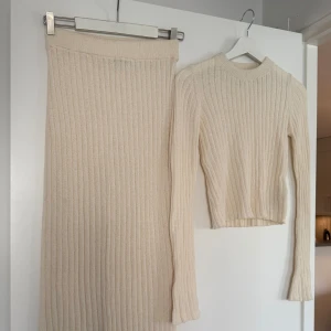 Beige ribbstickad tröja Gina Tricot - Supermjuk och ribbstickad set från Gina Tricot. Tröjan har lång ärm, rund halsringning och en lite kortare modell. Kjolen är low waist men går att styla på olika sätt! Strl s på kjol och xs på tröjan🤩