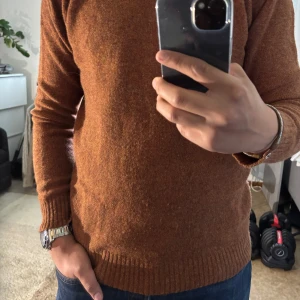 Brun stickad tröja från GANT Rugger - Säljer en brun stickad tröja från GANT Rugger i storlek L. Tröjan har rund halsringning, ribbade muddar och är tillverkad i ull. Perfekt för dig som gillar klassisk stil med en touch av vintage. Passar snyggt till jeans eller chinos.