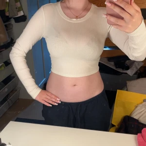 Ribbad croppad långärmad topp - Snygg croppad topp i ljusbeige med ribbad struktur och långa ärmar. Perfekt för dig som gillar en enkel men trendig stil. Mjuk och stretchig, sitter tajt och framhäver figuren. Rund halsringning och stilren look.