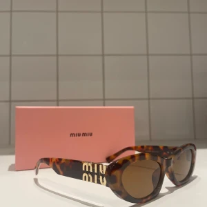 Miu Miu cat eye solglasögon leopard - Snygga cat eye solglasögon från Miu Miu med leopardmönstrad båge i brunt och guldiga detaljer på sidorna. Modellen är MU 09YS och har bruna glas. Perfekt accessoar för att lyfta din stil.